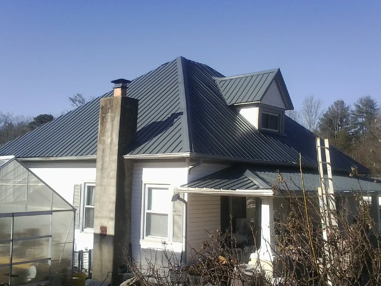 Dark blue standing seam metal roof on a white farmhouse with dormer — Slate & Tile Roof Repair by Roofing Brothers in Hiltons