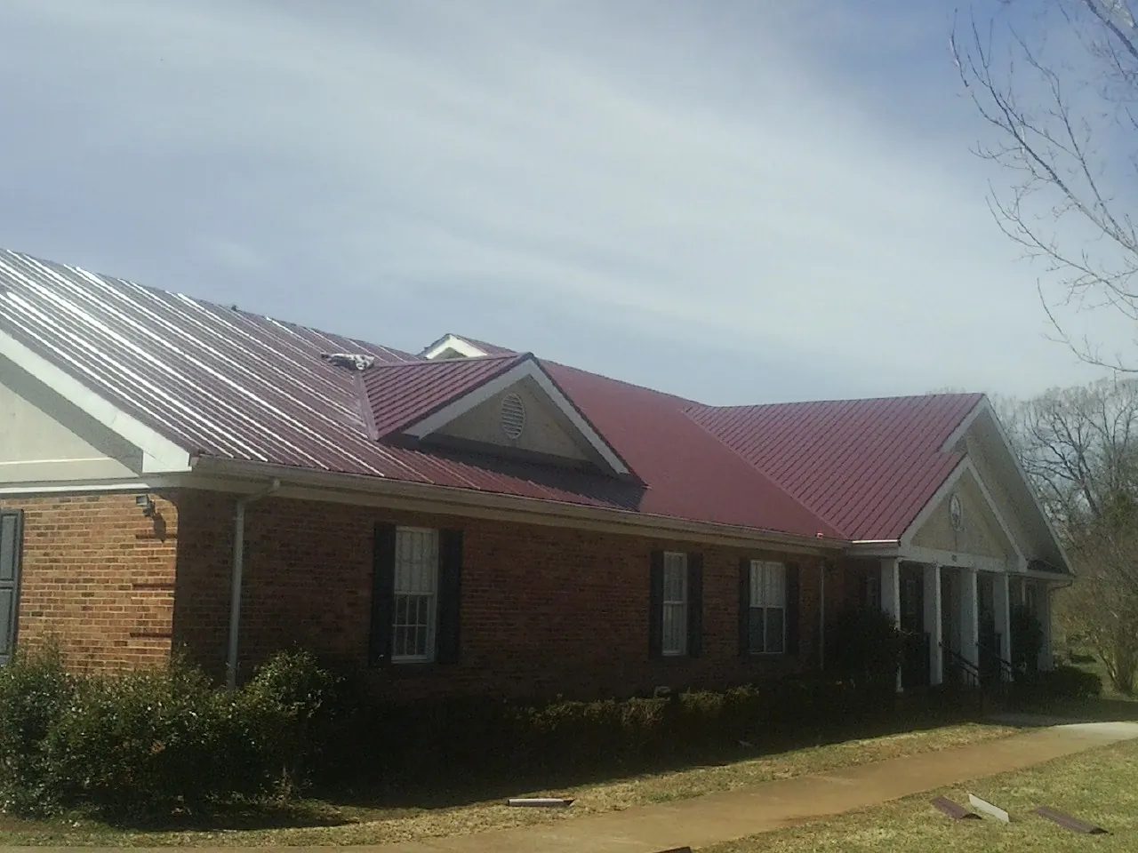 Red metal roof with gabled entries on a long brick building, from a Hail Damage Roof Repair job in Hiltons