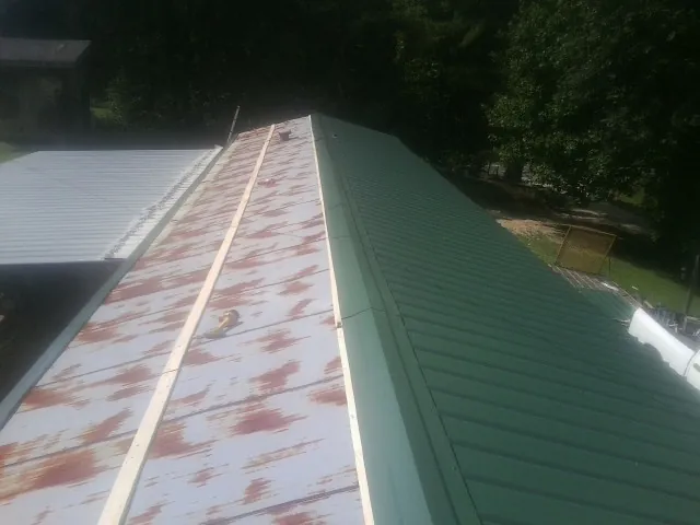 Old rusted panels beside newly installed green metal roofing — Wind Damage Roof Repair by Roofing Brothers in Hiltons