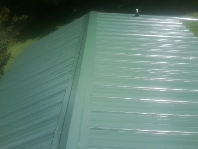 New green metal panels meeting at the ridge of a roof — Flat Roof Repair work by our crew in Hiltons
