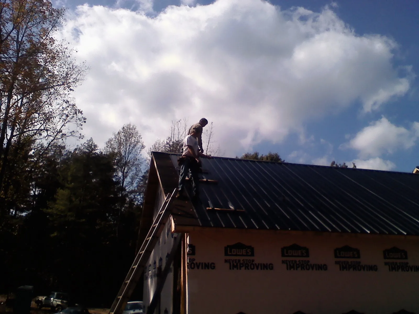 Roofer fastening dark metal panels high against a cloudy sky, from a Roof Inspection job in Hiltons