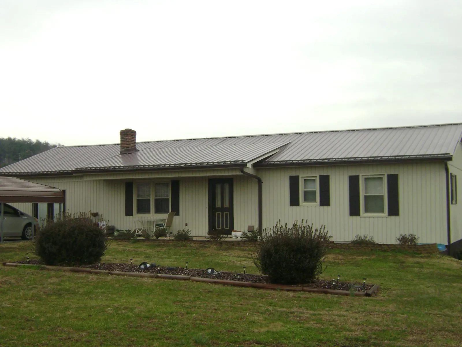 Brown metal roof on a cream sided ranch home with a brick chimney in Hiltons