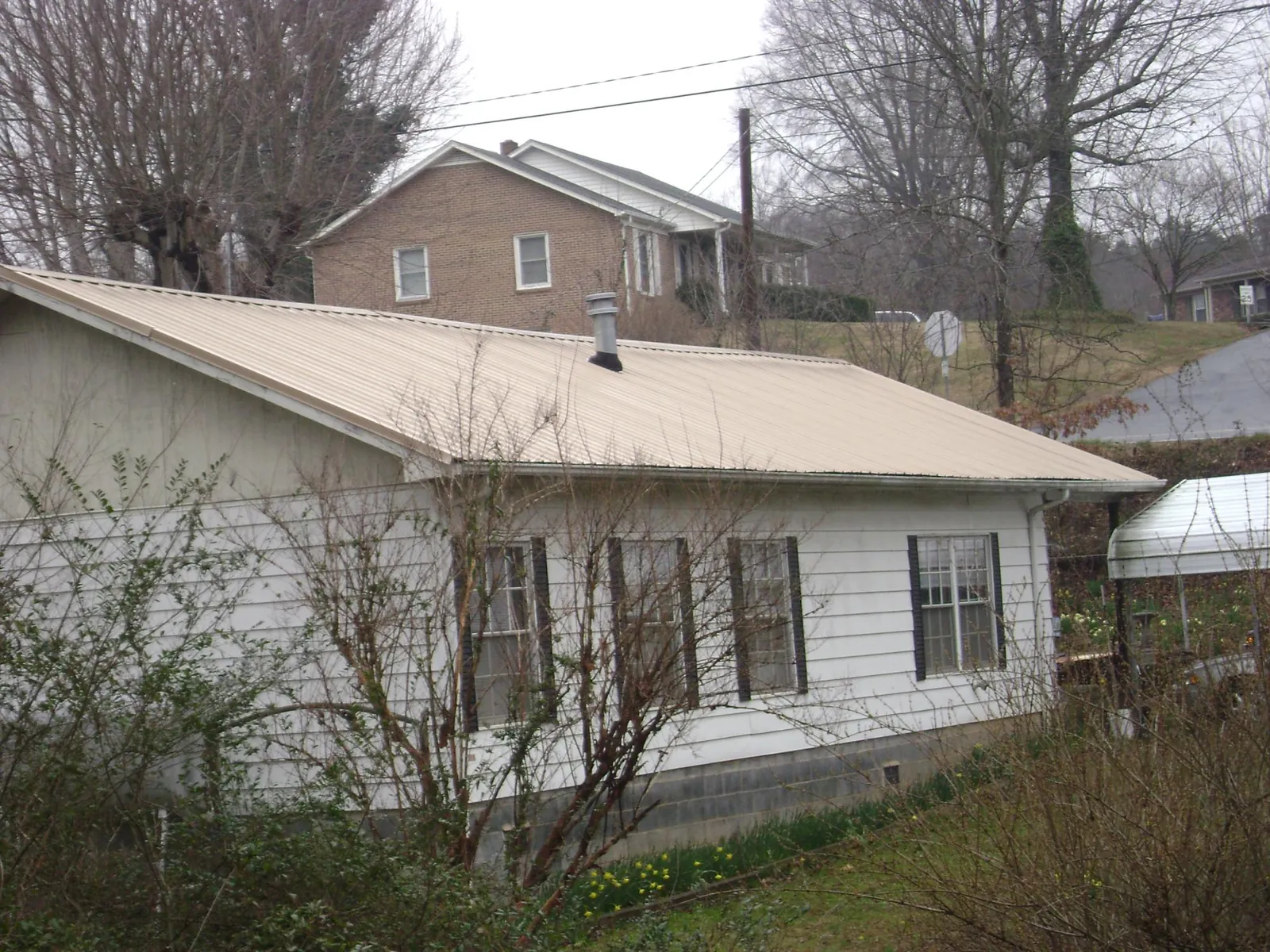Tan metal roof on a white sided house set into a hillside — Commercial Roofing by Roofing Brothers in Hiltons